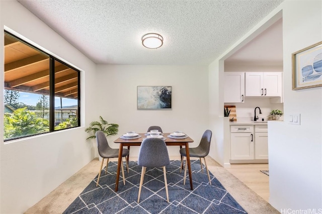 dining area featuring beamed ceiling, a textured ceiling, light colored carpet, and sink