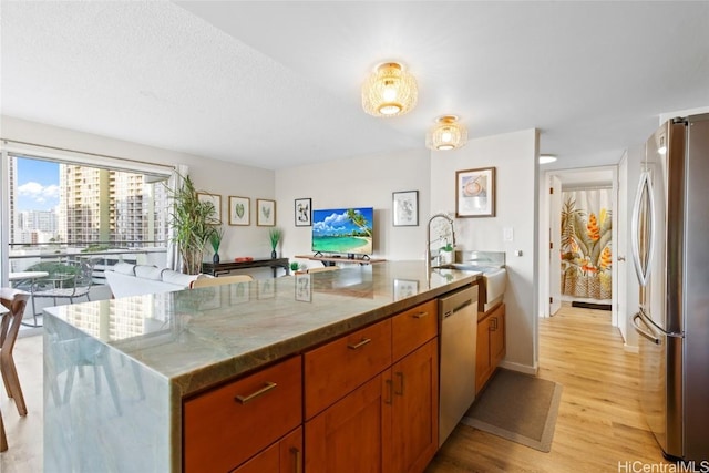 kitchen with light stone countertops, light wood-type flooring, stainless steel appliances, and sink