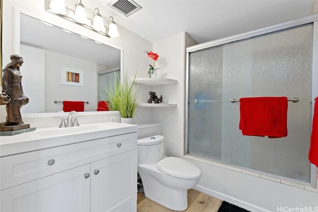 full bathroom featuring vanity, wood-type flooring, combined bath / shower with glass door, and toilet