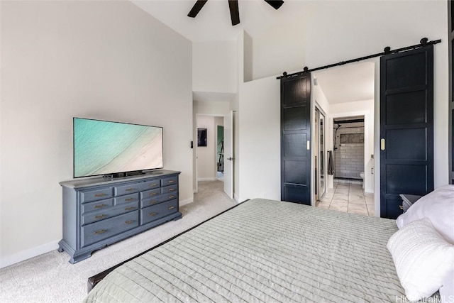 carpeted bedroom with ceiling fan, ensuite bath, a barn door, and high vaulted ceiling