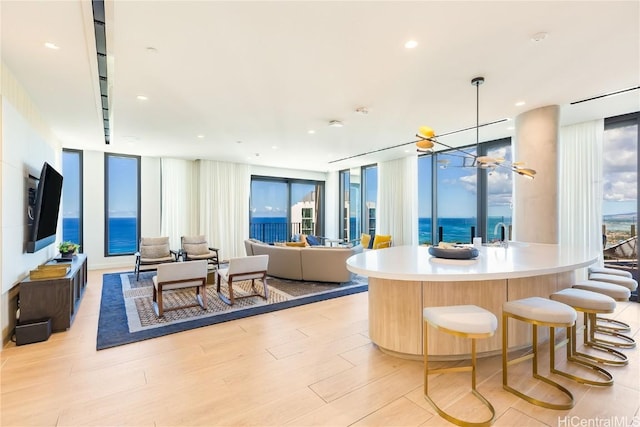 kitchen with expansive windows, pendant lighting, an inviting chandelier, light hardwood / wood-style flooring, and an island with sink