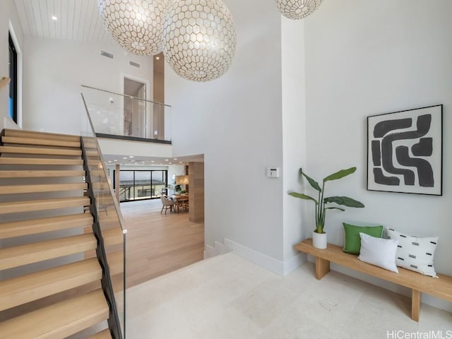 stairs featuring a notable chandelier, wood-type flooring, and a high ceiling