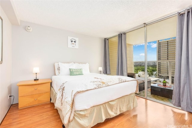 bedroom featuring access to exterior, a textured ceiling, hardwood / wood-style flooring, and floor to ceiling windows