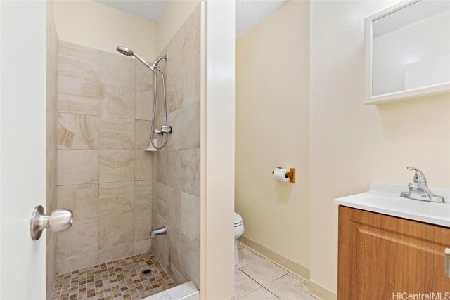 bathroom with tile patterned floors, a textured ceiling, vanity, tiled shower, and toilet