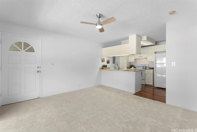 kitchen featuring ceiling fan, kitchen peninsula, a textured ceiling, white appliances, and carpet