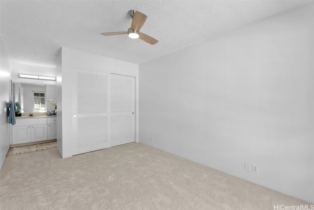 unfurnished bedroom featuring light carpet, a textured ceiling, a closet, and ceiling fan