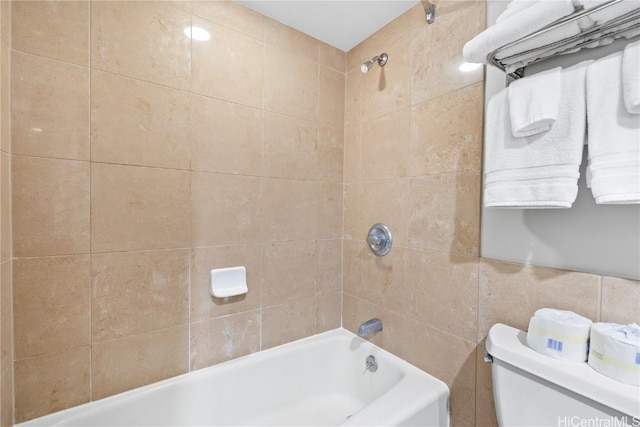 bathroom featuring tiled shower / bath combo, toilet, and tile walls