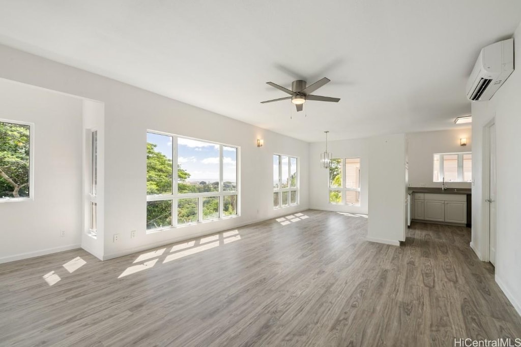 unfurnished living room featuring sink, ceiling fan with notable chandelier, wood-type flooring, and an AC wall unit