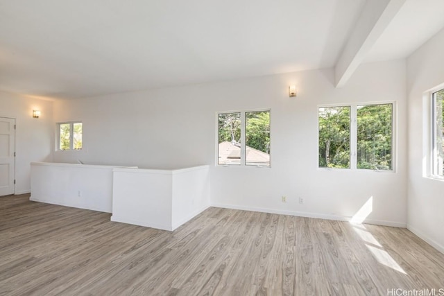 empty room with beam ceiling, plenty of natural light, and light hardwood / wood-style flooring