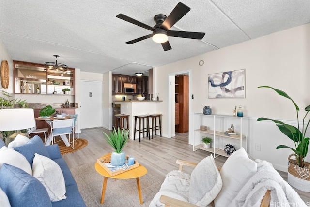 living room with ceiling fan, a textured ceiling, and light wood-type flooring