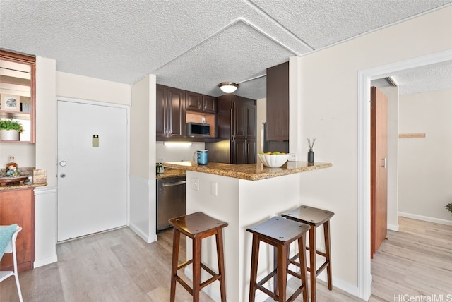 kitchen featuring a kitchen breakfast bar, light wood-type flooring, a textured ceiling, and appliances with stainless steel finishes