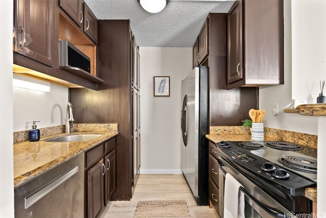 kitchen with light stone countertops, appliances with stainless steel finishes, a textured ceiling, dark brown cabinetry, and sink