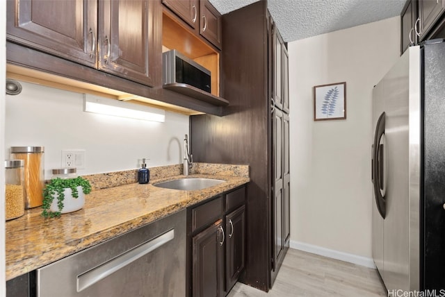 kitchen with dark brown cabinetry, sink, light stone counters, stainless steel fridge, and a textured ceiling