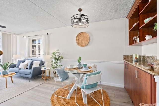 dining space with light hardwood / wood-style flooring, a textured ceiling, and an inviting chandelier