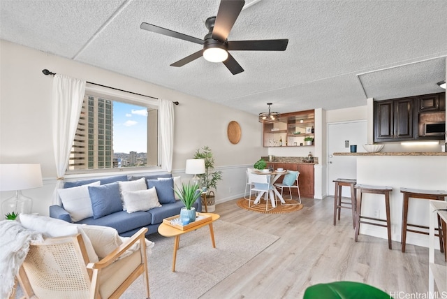 living room featuring ceiling fan, light wood-type flooring, and a textured ceiling