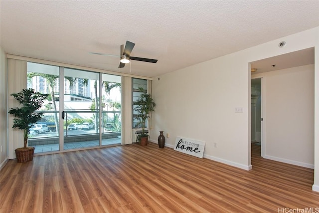 empty room with floor to ceiling windows, hardwood / wood-style floors, a textured ceiling, and ceiling fan