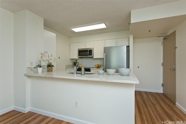 kitchen with white cabinets, kitchen peninsula, hardwood / wood-style floors, and appliances with stainless steel finishes