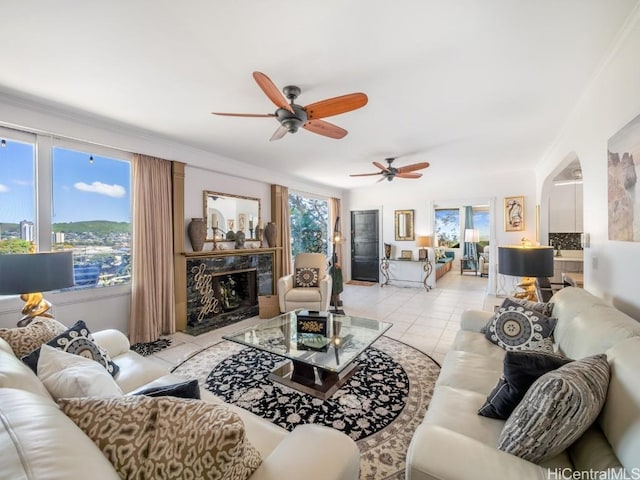 tiled living room with a high end fireplace, ornamental molding, ceiling fan, and a healthy amount of sunlight