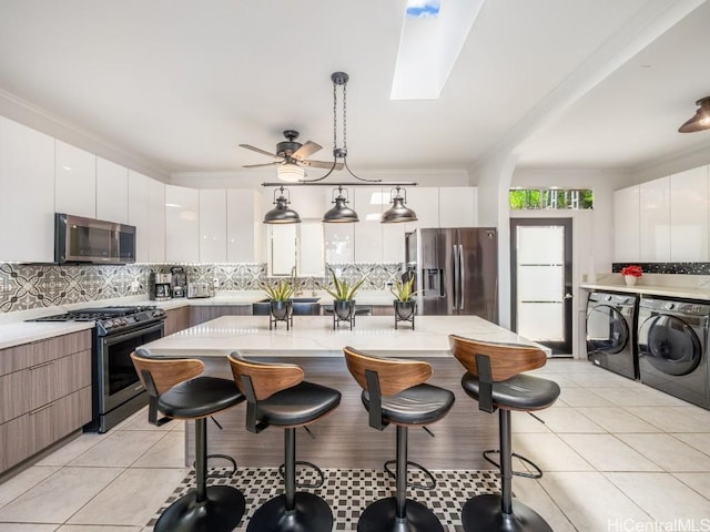 kitchen with stainless steel appliances, tasteful backsplash, washing machine and dryer, pendant lighting, and white cabinets