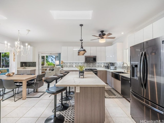 kitchen with a skylight, a center island, decorative light fixtures, white cabinets, and appliances with stainless steel finishes