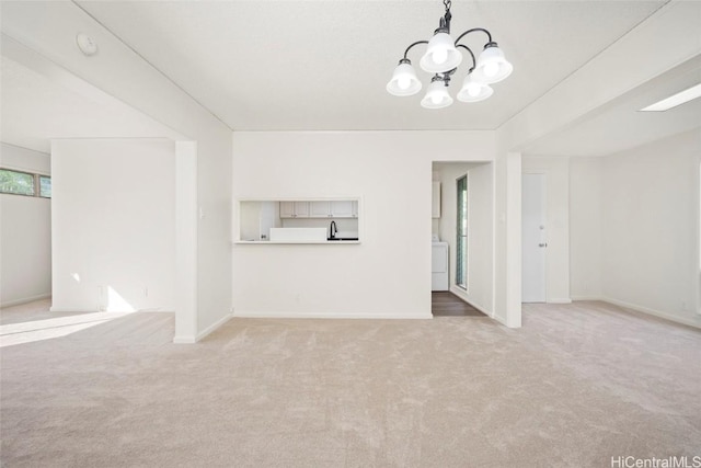 unfurnished living room featuring carpet flooring, washer / dryer, and a chandelier