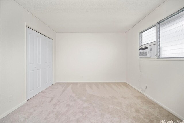 unfurnished bedroom with a closet, cooling unit, light colored carpet, and a textured ceiling