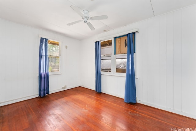 empty room featuring ceiling fan, dark wood-type flooring, and wood walls