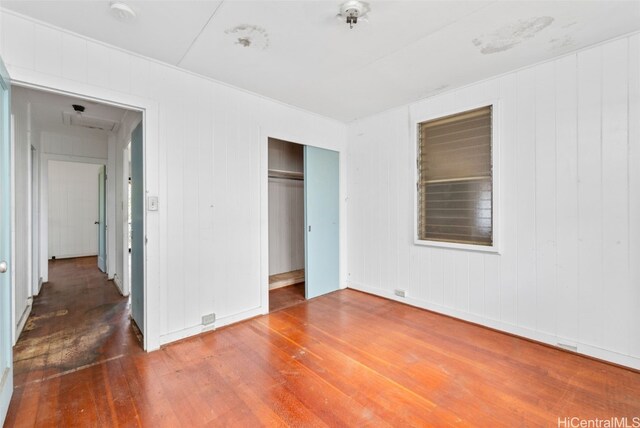 unfurnished bedroom with wood-type flooring, wooden walls, and a closet