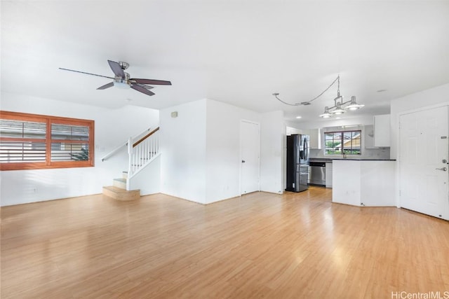 unfurnished living room featuring light hardwood / wood-style flooring and ceiling fan with notable chandelier