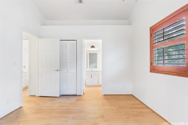 unfurnished bedroom featuring ensuite bathroom, light hardwood / wood-style floors, and a closet