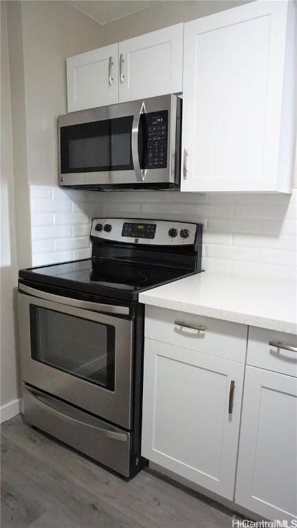 kitchen with appliances with stainless steel finishes, backsplash, wood-type flooring, and white cabinetry