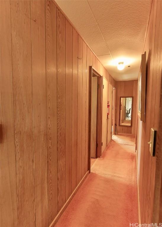 corridor featuring a textured ceiling, wood walls, and light carpet