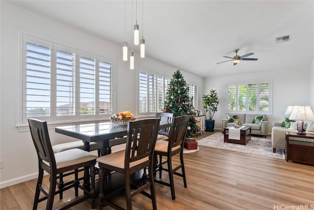 dining area with ceiling fan with notable chandelier, a healthy amount of sunlight, and light wood-type flooring