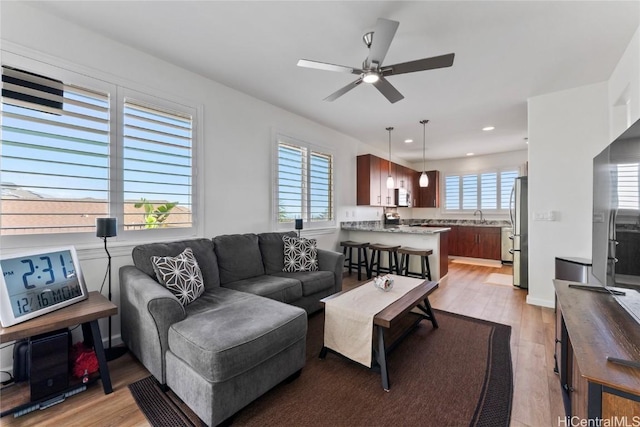 living room with light wood-type flooring, ceiling fan, and sink