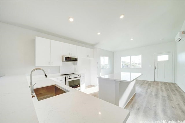 kitchen featuring white range with electric cooktop, stainless steel microwave, an AC wall unit, light wood-type flooring, and a sink