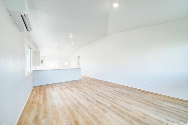 empty room with light hardwood / wood-style flooring, lofted ceiling, and a wall unit AC