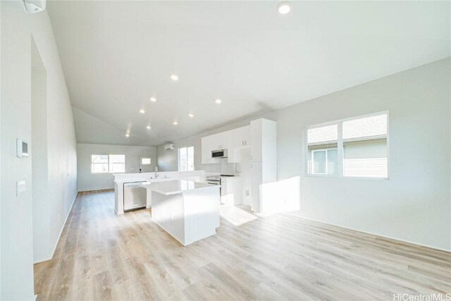 kitchen with white cabinets, vaulted ceiling, appliances with stainless steel finishes, light hardwood / wood-style floors, and kitchen peninsula