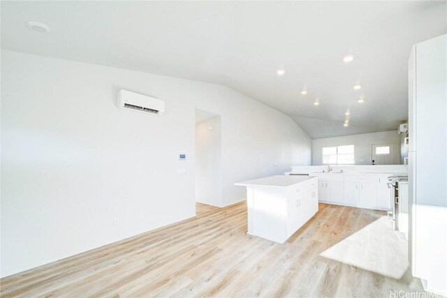 kitchen featuring light wood-type flooring, vaulted ceiling, a wall mounted AC, white cabinets, and a center island