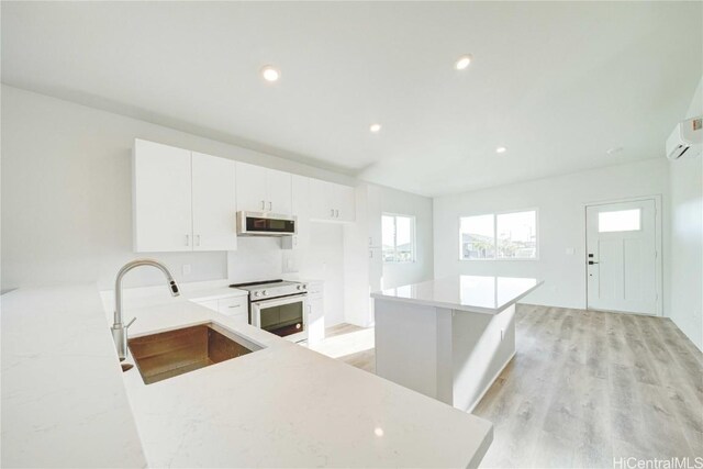 kitchen with light wood-type flooring, white electric range oven, sink, white cabinets, and a kitchen island