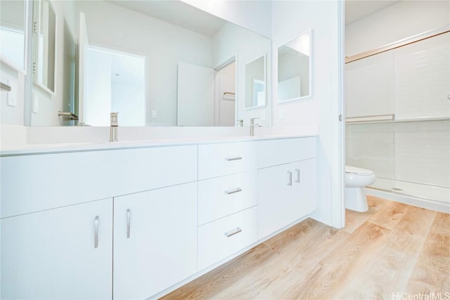 bathroom with toilet, vanity, an enclosed shower, and hardwood / wood-style flooring