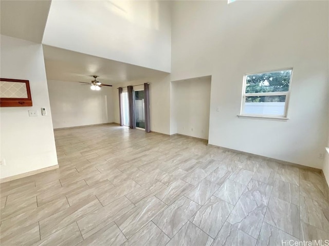 unfurnished living room featuring ceiling fan and a towering ceiling