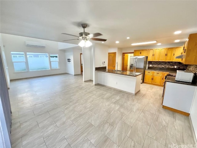 kitchen featuring backsplash, stainless steel refrigerator with ice dispenser, ceiling fan, kitchen peninsula, and a wall unit AC