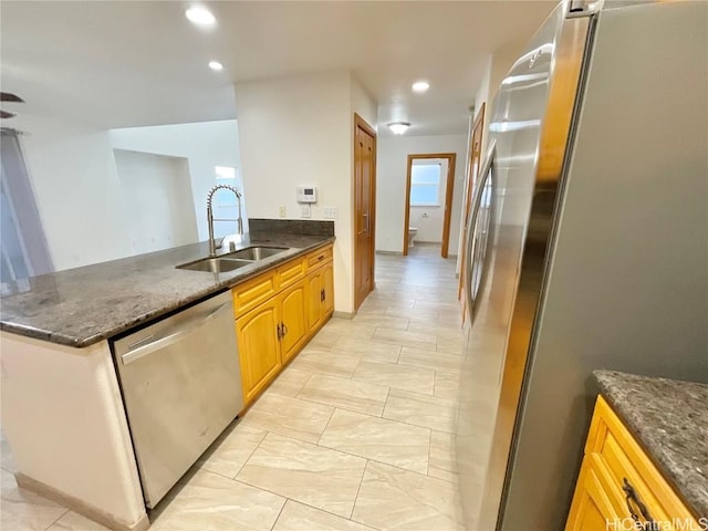 kitchen featuring kitchen peninsula, appliances with stainless steel finishes, dark stone countertops, and sink