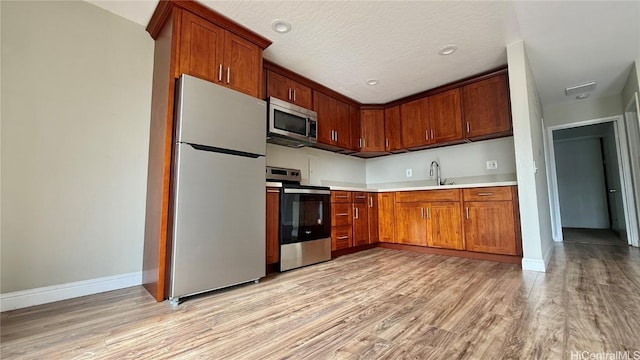 kitchen with appliances with stainless steel finishes, a textured ceiling, light hardwood / wood-style floors, and sink