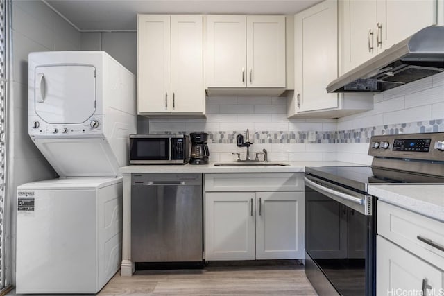 kitchen with stacked washing maching and dryer, stainless steel appliances, sink, light hardwood / wood-style floors, and white cabinetry