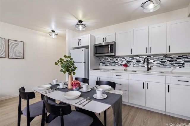 kitchen featuring white cabinets, stainless steel microwave, freestanding refrigerator, light countertops, and a sink