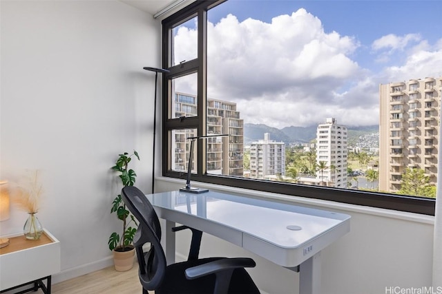 office area with light wood-style floors, baseboards, a mountain view, and a city view