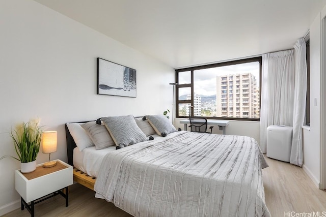 bedroom featuring light wood-style floors, a view of city, and baseboards