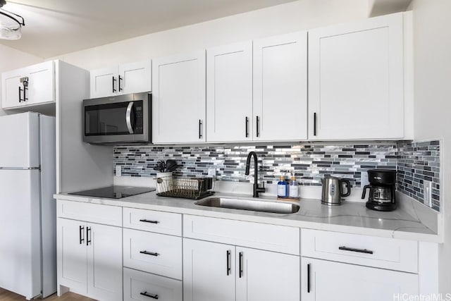 kitchen with stainless steel microwave, decorative backsplash, freestanding refrigerator, white cabinetry, and a sink