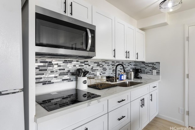 kitchen with light stone counters, black electric stovetop, white cabinetry, freestanding refrigerator, and stainless steel microwave